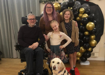 A family stood in front of party balloons with canine partner yellow lab at the front of the group