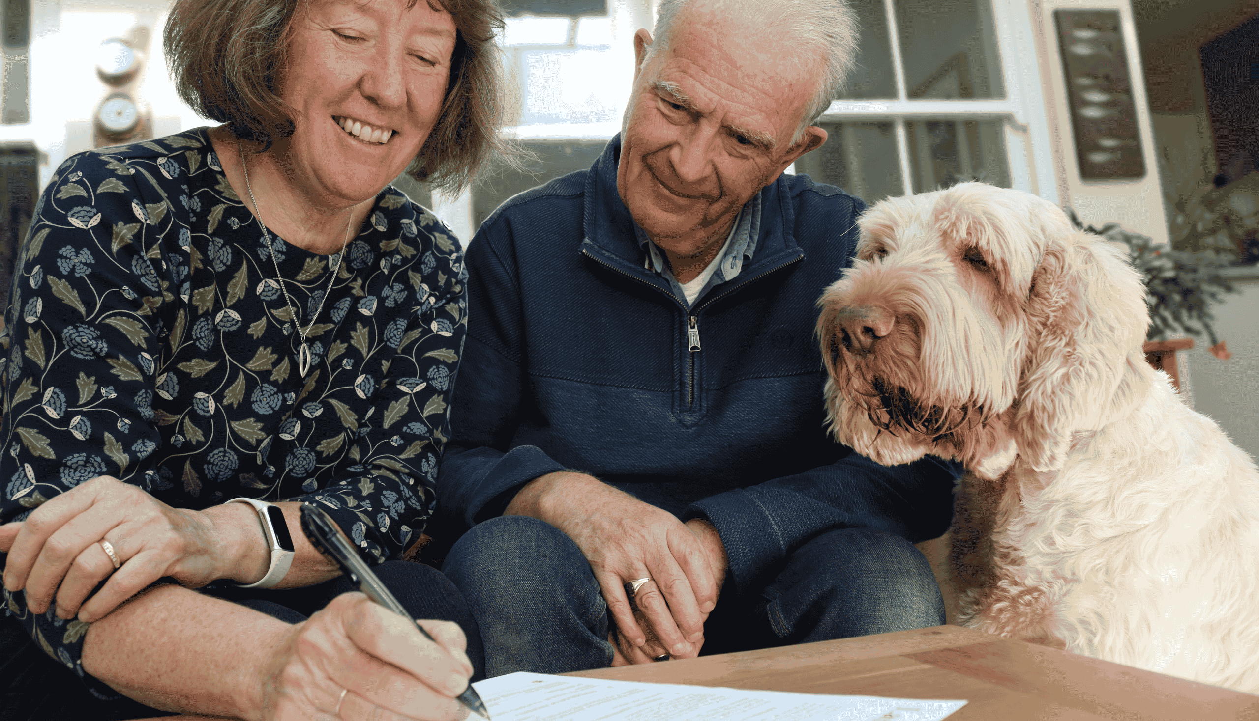 A woman signing her will, with her husband and a dog look on.