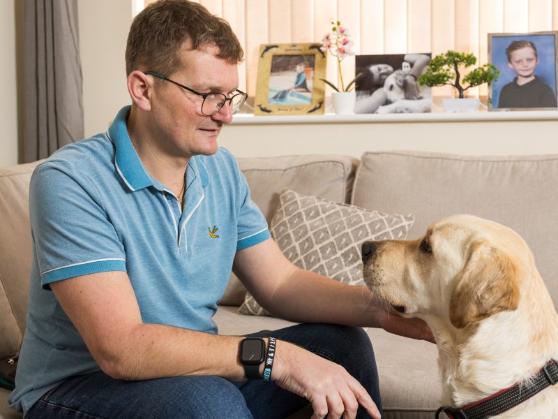Rob sat on a sofa looking at his Canine Partner Eddy