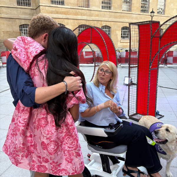 Lady hugging a man whilst speaking to lady in wheelchair with her dog next to her