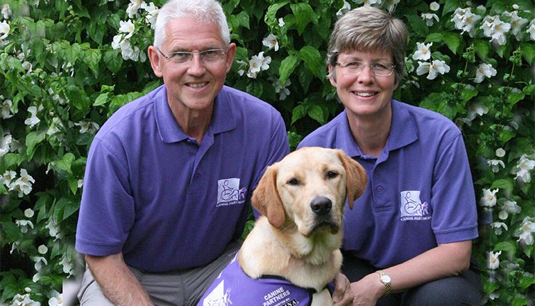 Two puppy parents posing with a Canine Partner in training. Puppy parents socialise the puppies before they start advanced training