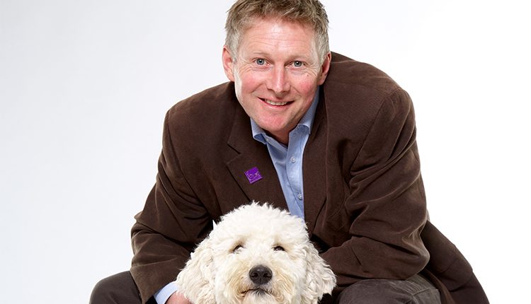 Canine Partners CEO Andy Cook posting with white poodle cross dog