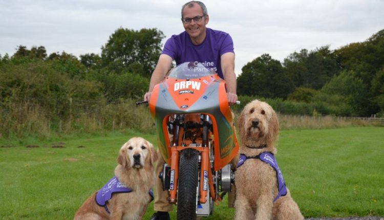 Daredevil Phil posing on electric motorbike with two Canine Partners dogs