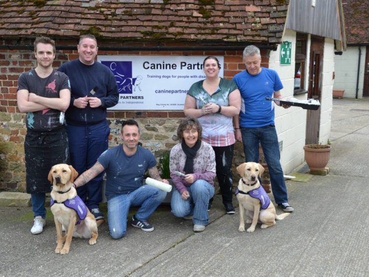 Greggs team stood in front of Canine Partners sign with dogs