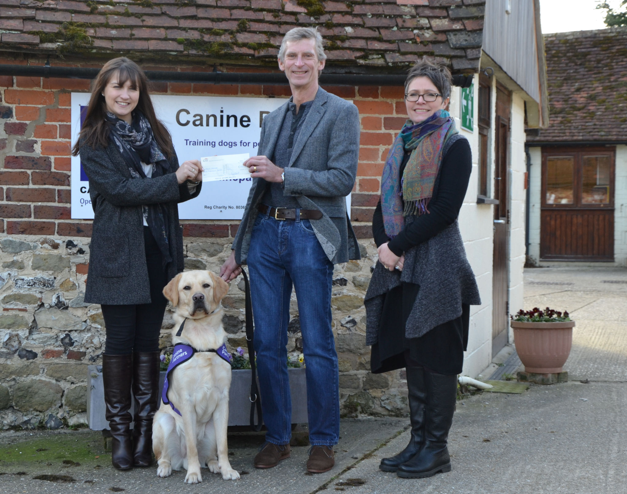 Members of the Income Generation Team and a dog in training at Canine Partners receiving a cheque from a Charitable Trust