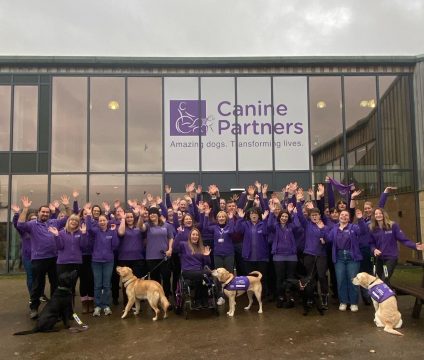 Canine partners staff smiling with their hands up standing outside canine partners building