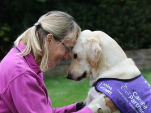 A guide dog and a smiling individual in close contact, looking into each other's eyes. The individual is smiling at the dog.